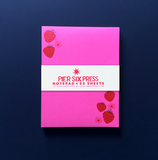 Pink notepad with strawberry design and 'Pier Six Press' branding on a dark blue background