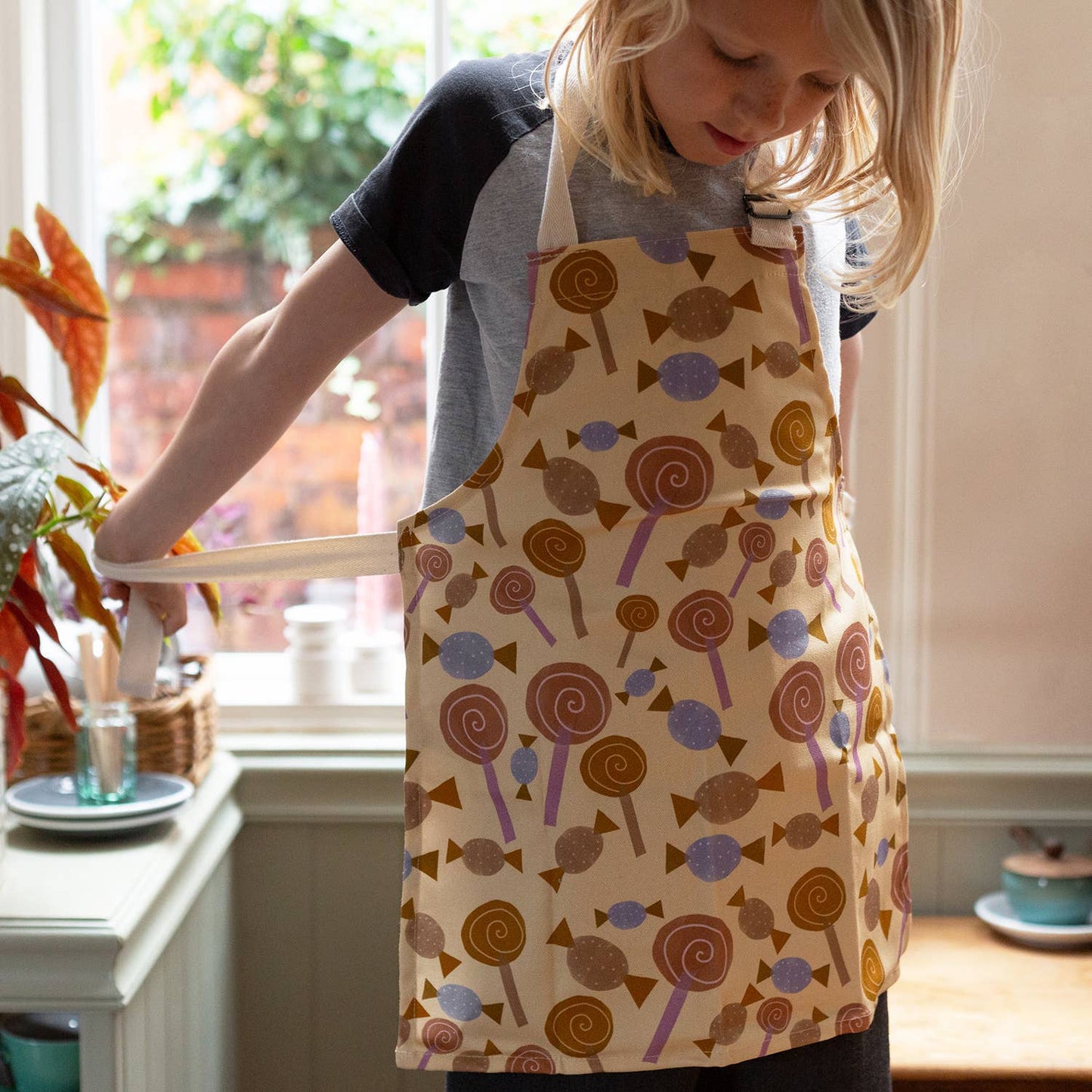 Child wearing an apron that has lollipops and candy on it. 