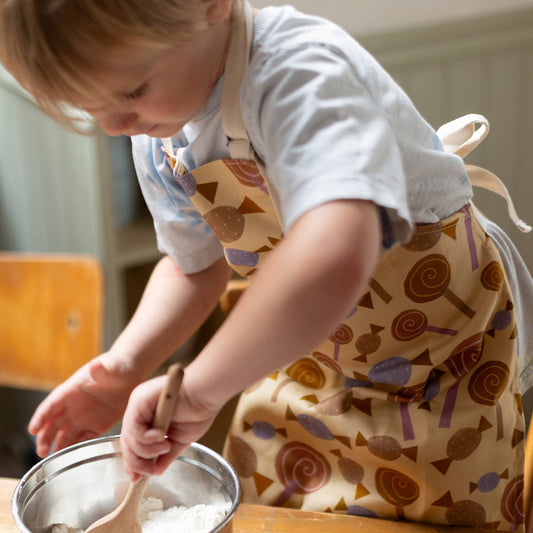 Child with candy patterned apron mixing a bowl of flour.