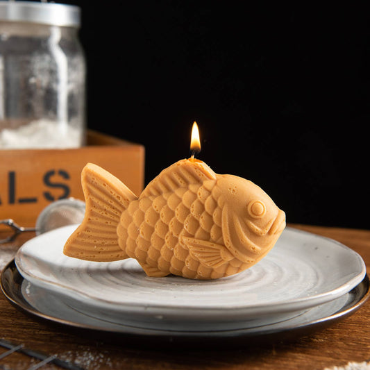Fish-shaped candle burning on a white plate with a dark background