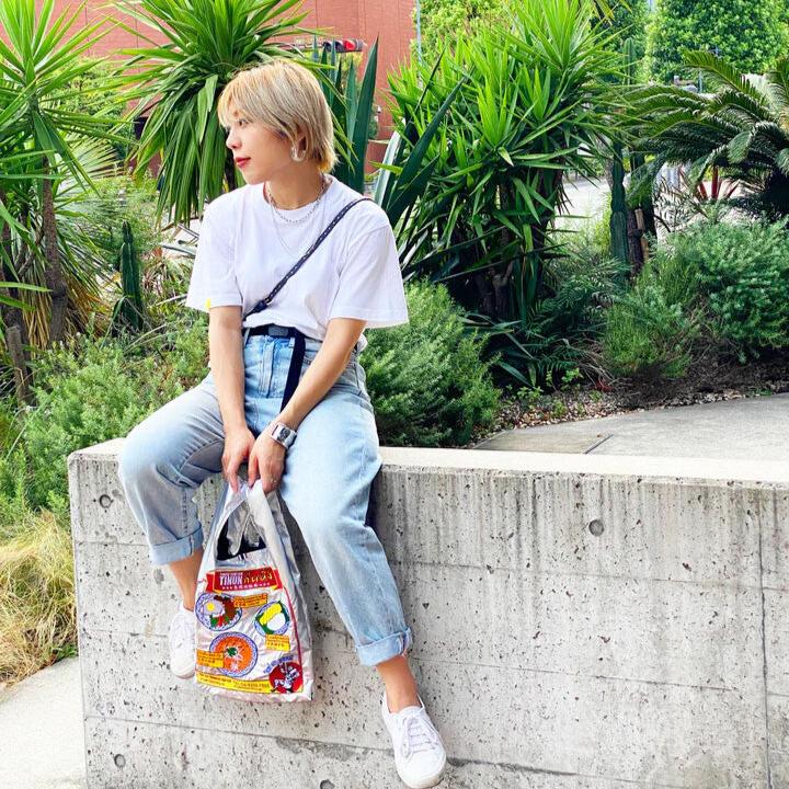 Silver bag featuring several popular Thai food dishes and text written in Thai. A Mui Thai boxer is on the bottom right.  Girl sitting on the wall modeling the bag.