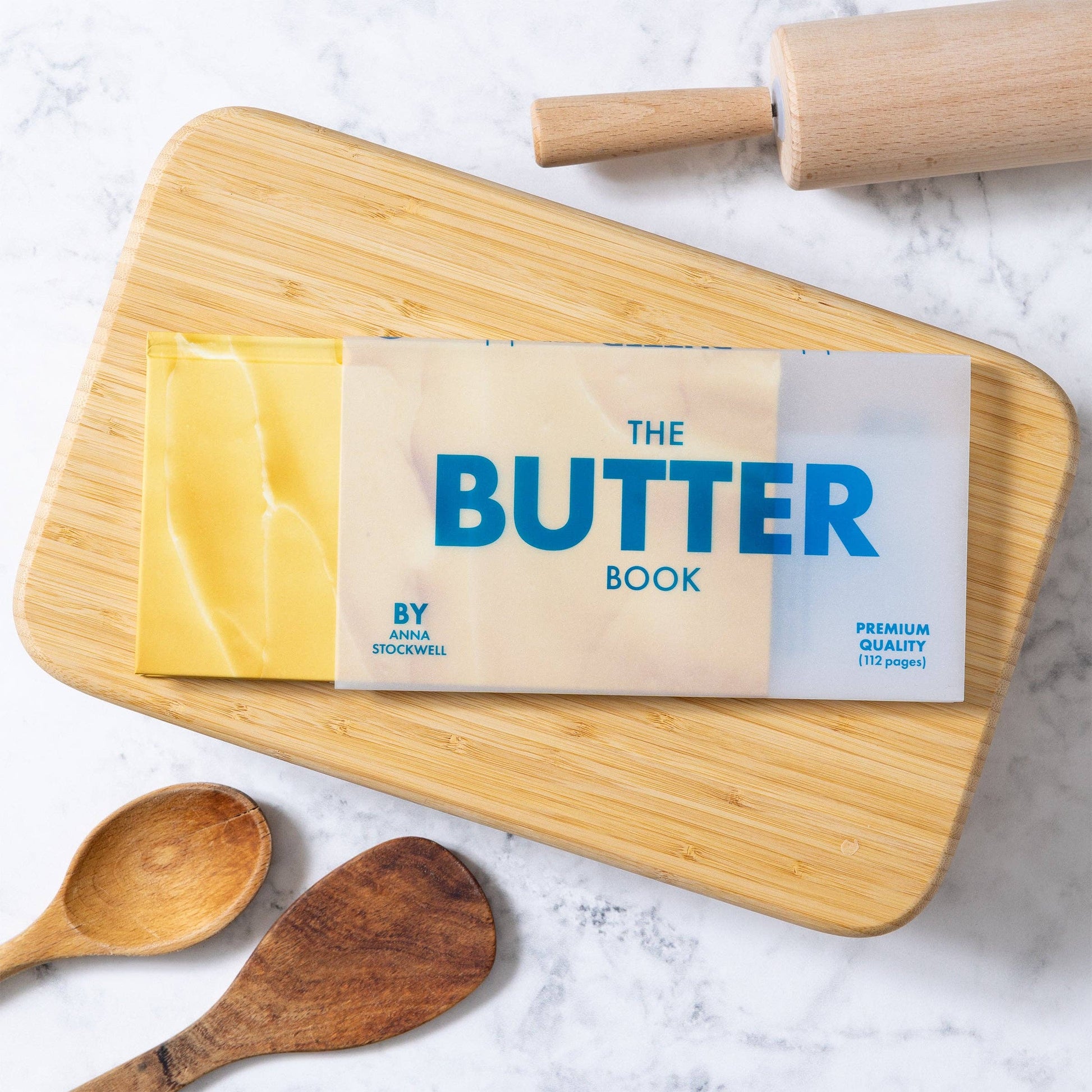 Butter Book packaging on a wooden cutting board with a rolling pin and wooden spoons.