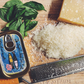 Closed tinned fish candle on a cutting board with basil leaves and grated cheese 