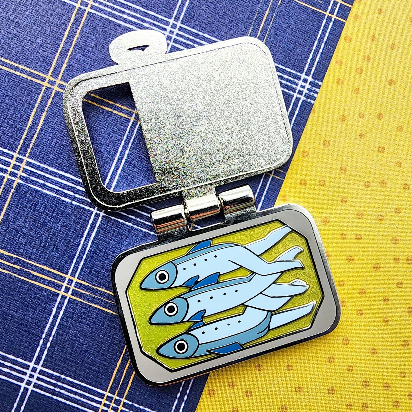 Tightly Packed Sardines Pin - metal pin shown in open position, full view of "inside" the tin where three sardines lie in oil with their anthropomorphic legs entwined.