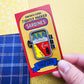 Tightly Packed Sardines Pin - metal pin shown in closed position and attached to colorful red, yellow and blue cardboard backing.