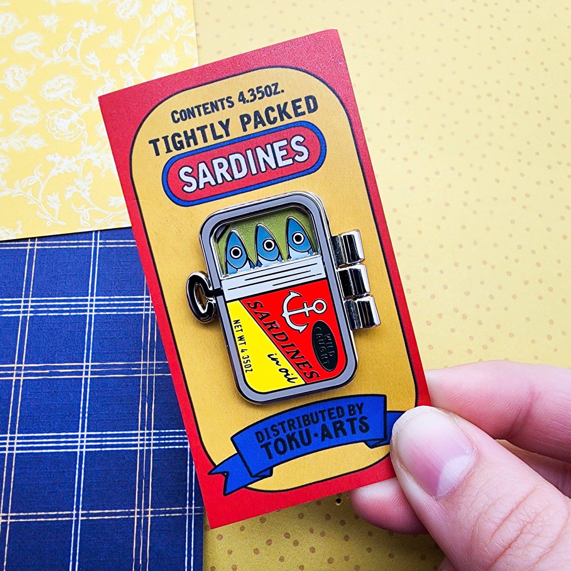 Tightly Packed Sardines Pin - metal pin shown in closed position and attached to colorful red, yellow and blue cardboard backing.