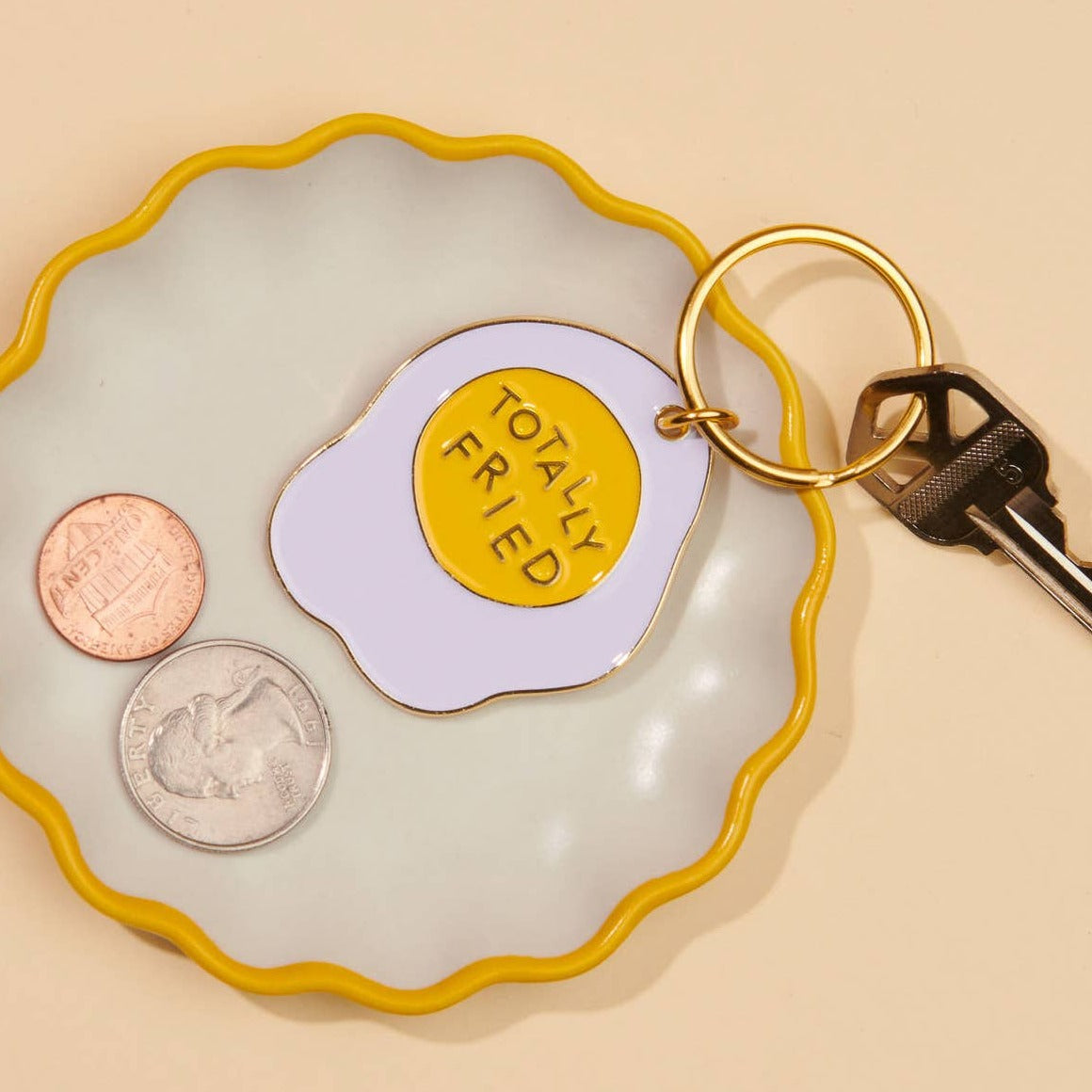 Totally Fried sunnyside up egg keychain sitting on a trinket tray with coins and keys.