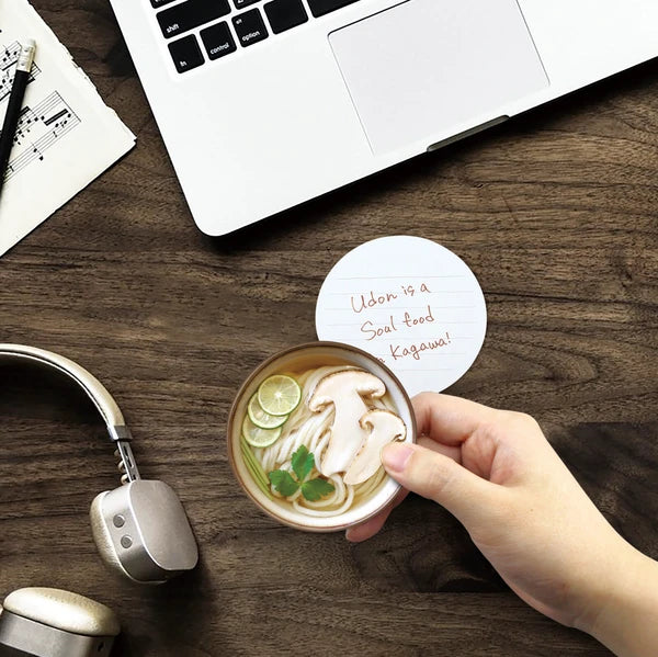 Staged udon memo pad at a computer desk. Writing on the back of the pad says: Udon is a soulfood of Kagawa.