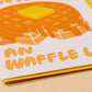 Close up of card that has waffles on it with syrup and butter. Yellow envelopes.