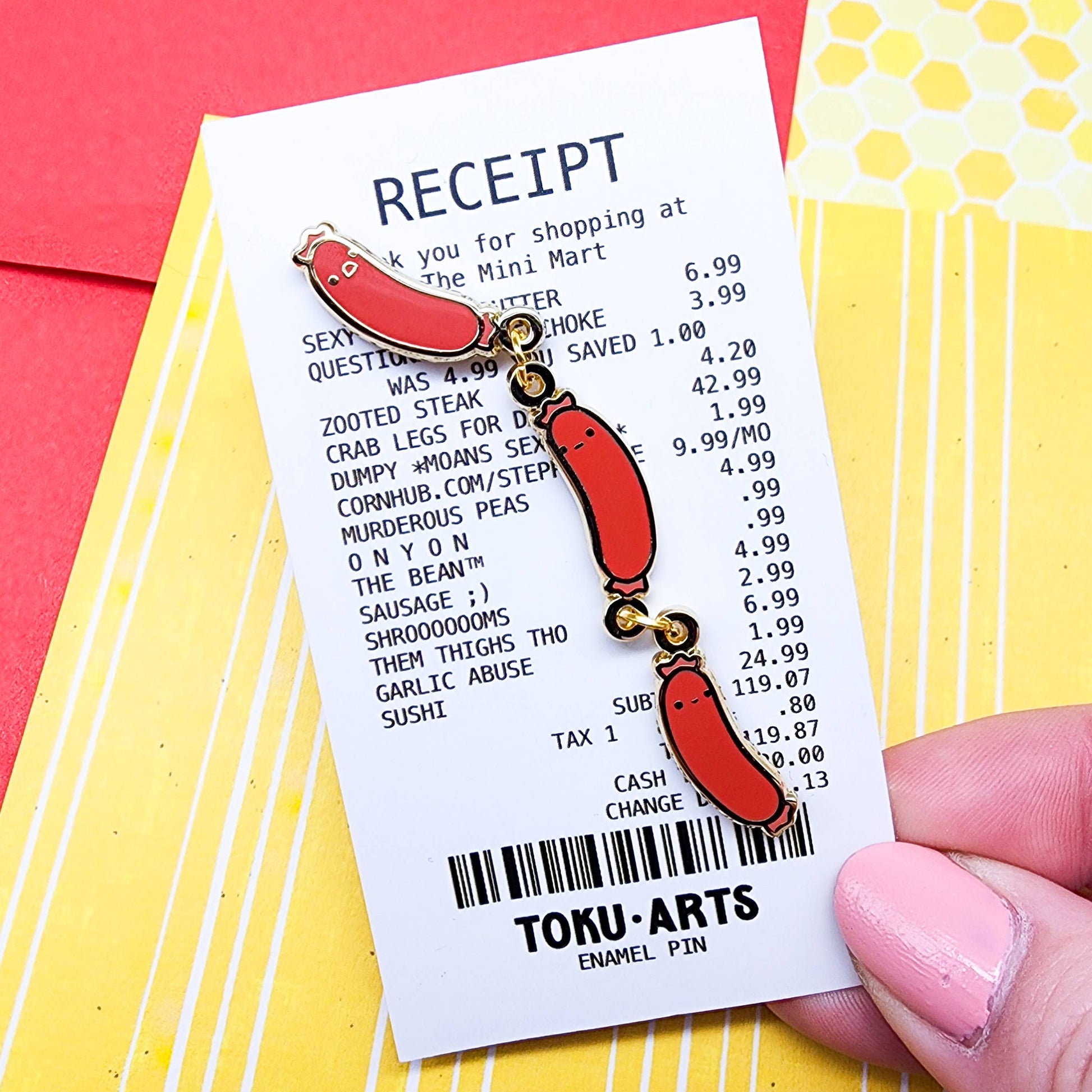 Photo of Weenies Pin - Metal pin with three red sausages, each with a cute little facial expression. Sausages are attached with gold metal o-rings. Shown on paper backing designed to look like a grocery receipt with a list of imaginary food items - be advised that "items" refer to mature/adult themes. Some examples include "Sexy Looking Butter," "Crab Legs for Days," "Murderous Peas," "Cornhub.com/Stepproduce," and "Shrooooooms."