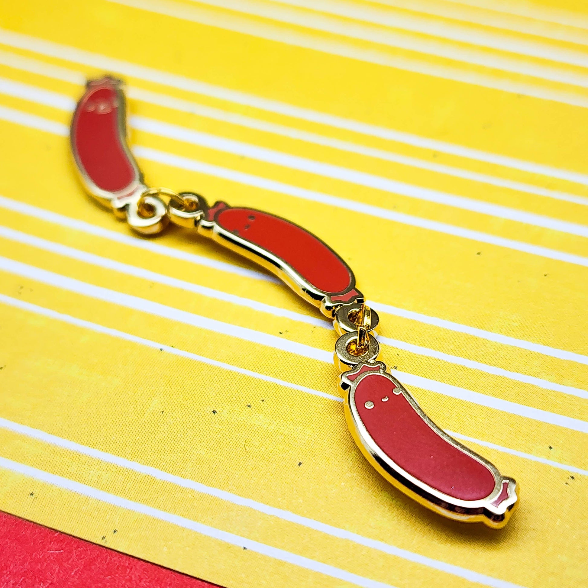 Photo of Weenies Pin - Metal pin with three red sausages, each with a cute little facial expression. Sausages are attached with gold metal o-rings.