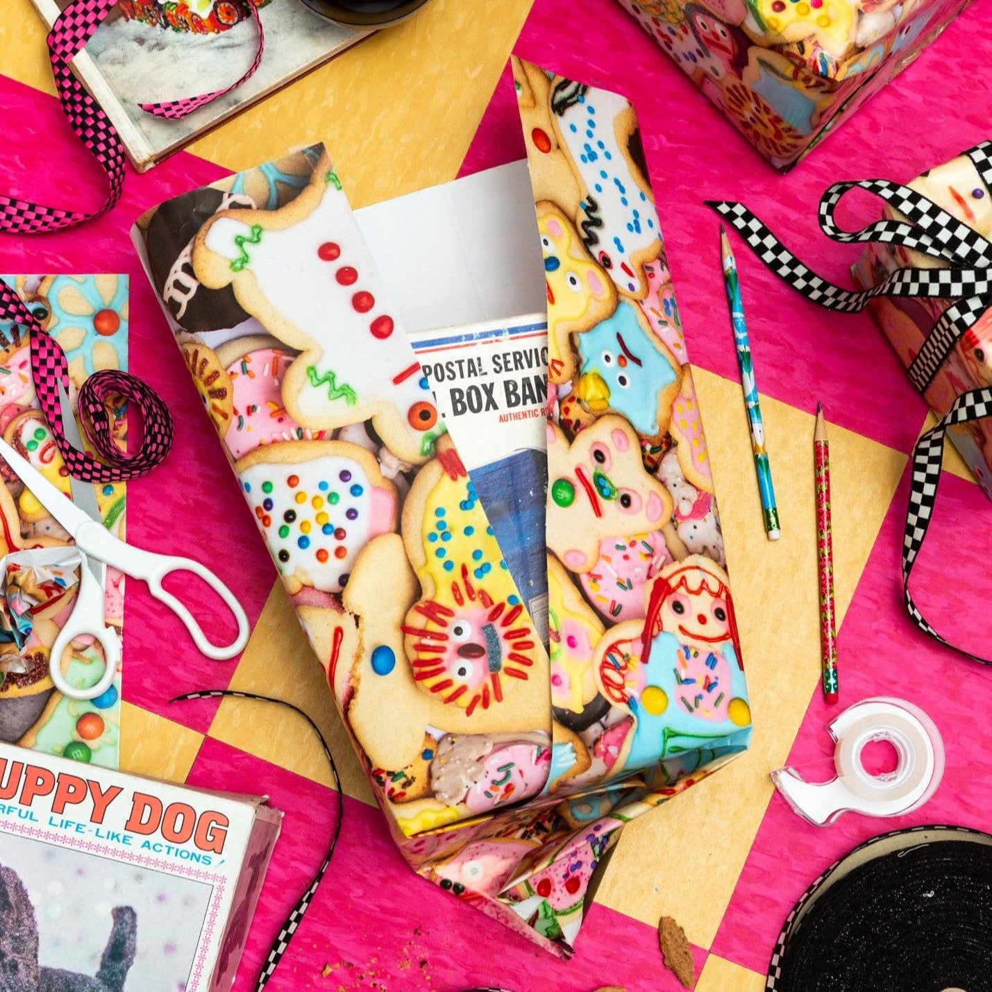 A table staged with lots of different knick-knacks to shot a box being wrapped by weird cookies gift wrap.