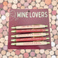 Set of pens with humorous wine-themed sayings on a card labeled 'Wine Lovers' against a colorful background.