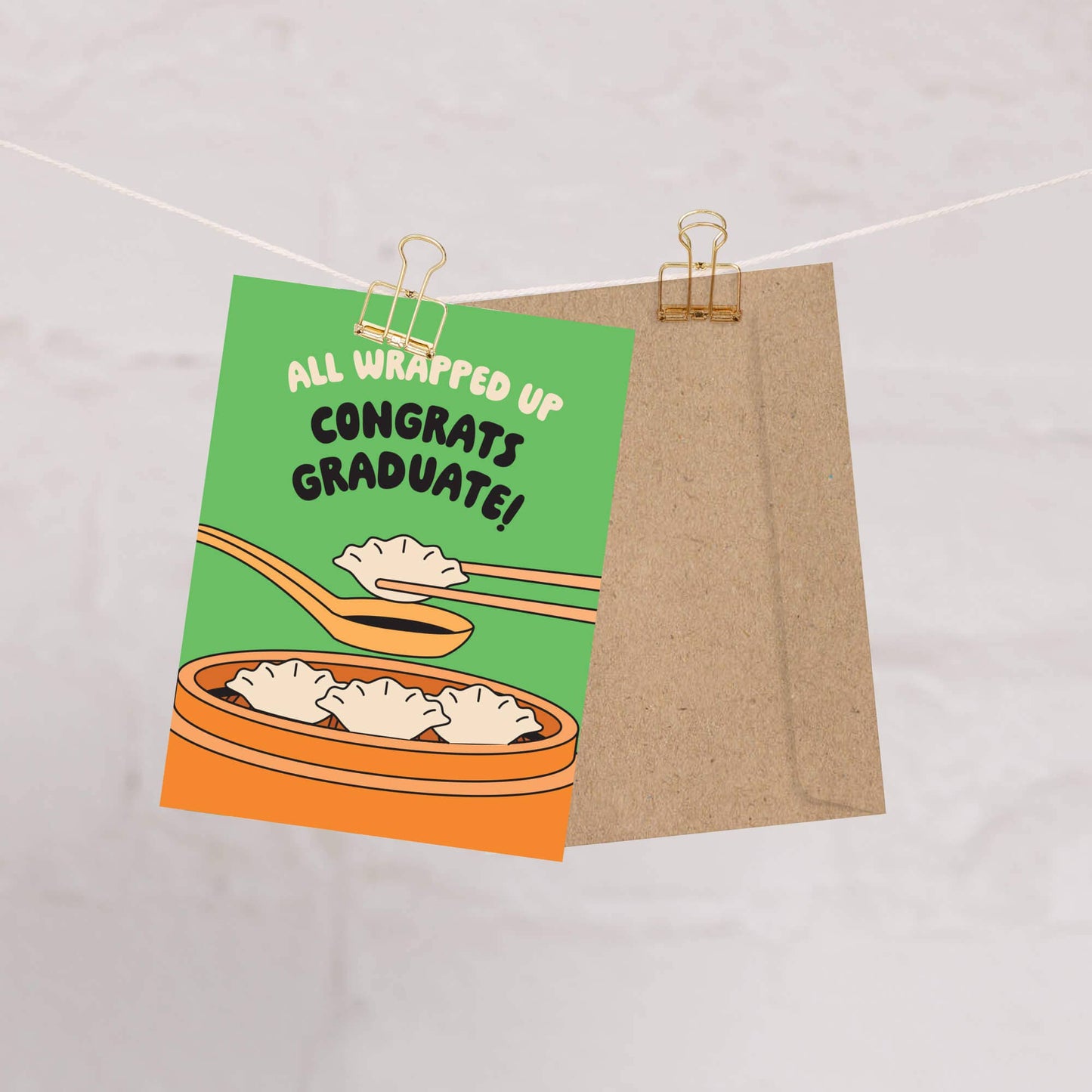 Graduation card with dumplings and text 'All wrapped up congrats graduate!' on a string.