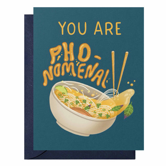A greeting card with a dark teal background and a navy envelope. The card features the text 'YOU ARE PHO-NOMENAL' in a playful yellow-orange font above an illustration of a bowl of noodle soup with chopsticks.