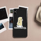 A black phone case featuring a cartoon butter character and the text 'You Butter Twerk.' displayed on a beige surface with scattered Polaroid-style photos and a partial white mug nearby.