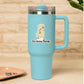 A light blue insulated travel tumbler with a handle, clear lid, and straw, featuring a cartoon butter stick graphic and the text 'You Butter Twerk.' on the front, set against a warm beige brick wall background.