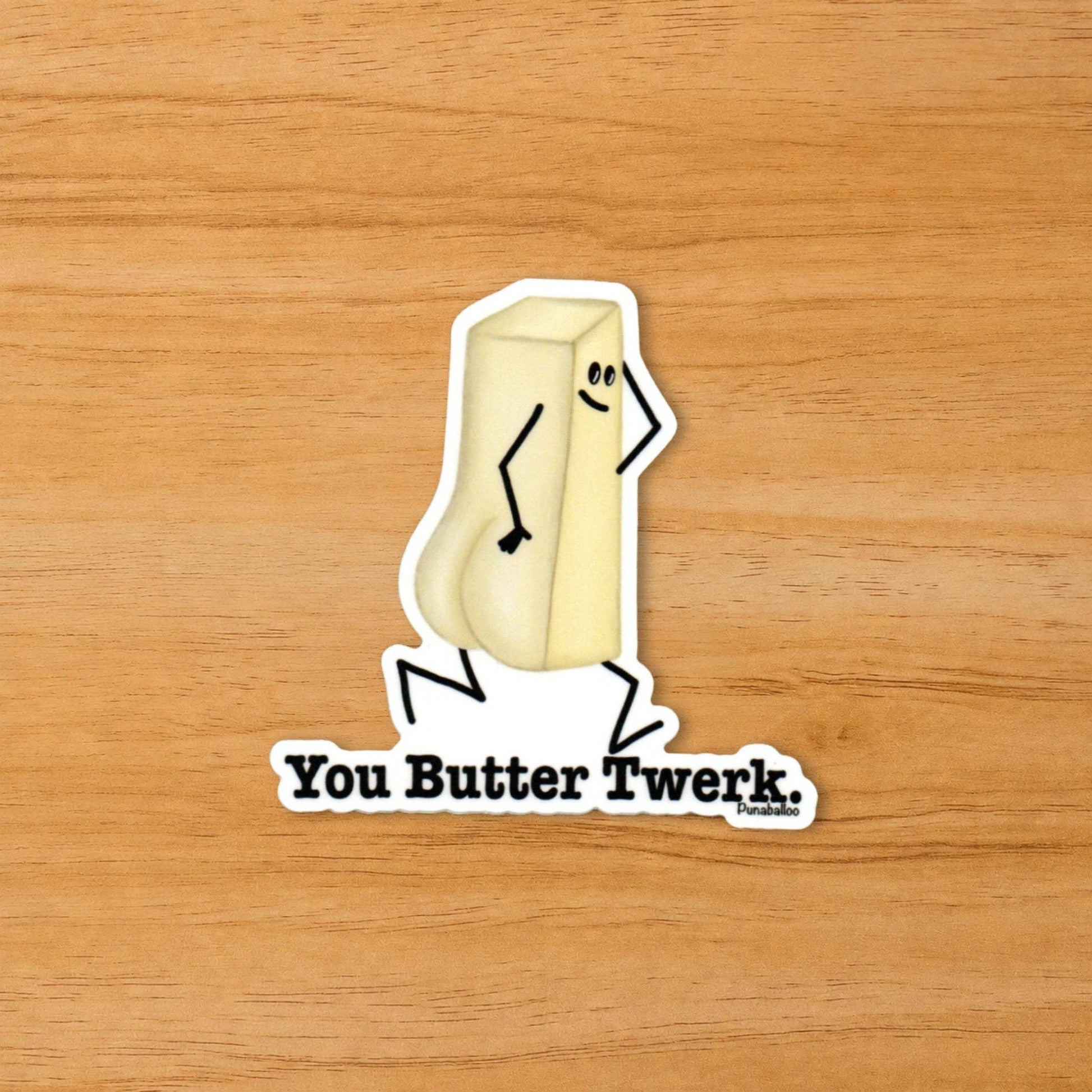 A die-cut sticker featuring a cartoon stick-figure-style butter block with the text 'You Butter Twerk.' on a light wood background.