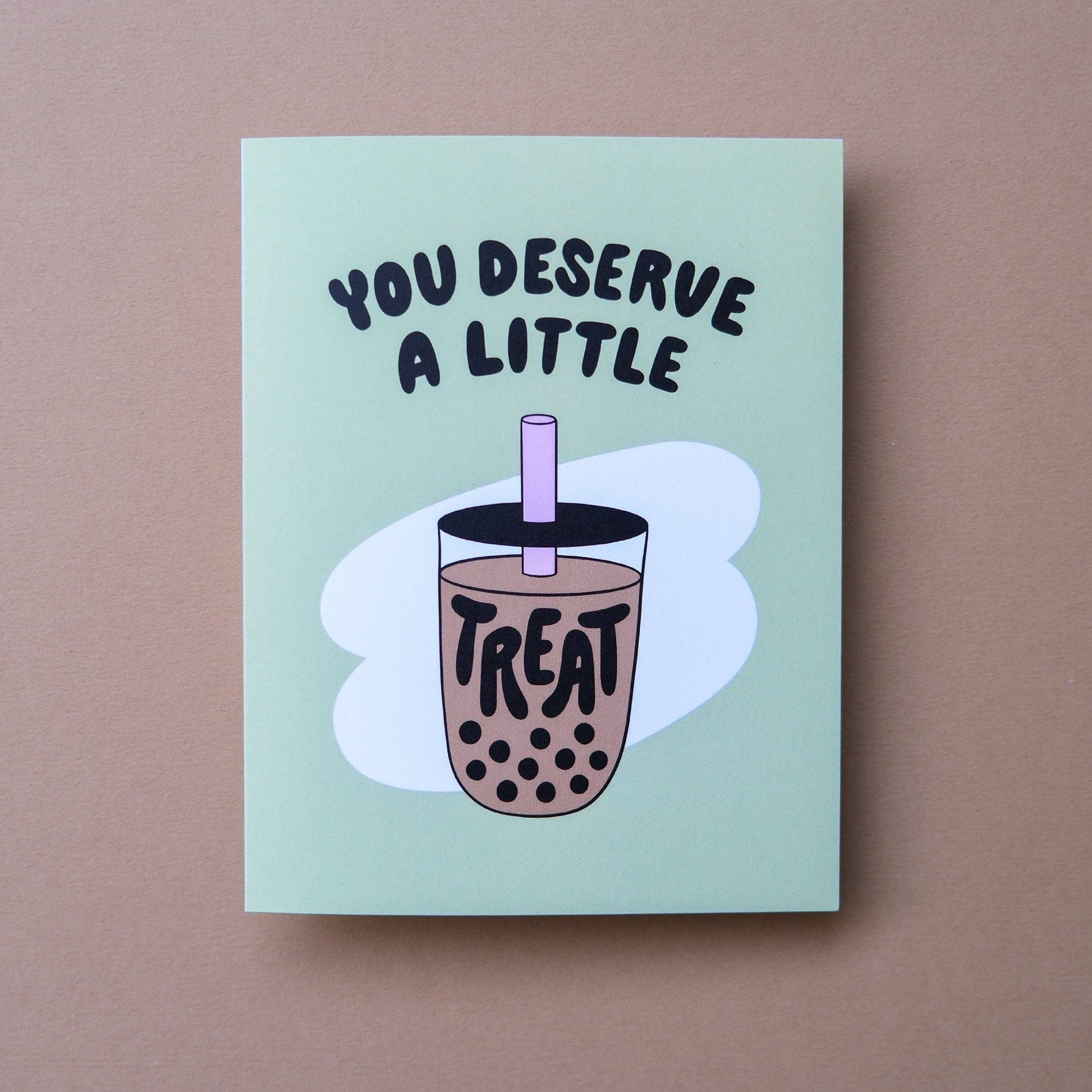 A square greeting card with a light mint green background, featuring the text 'YOU DESERVE A LITTLE' above an illustration of a bubble tea cup with the word 'TREAT' on it, set against a solid taupe background.