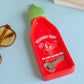 Red sriracha bottle-shaped trinket tray with a green cap on a light blue background, holding a ring and a key