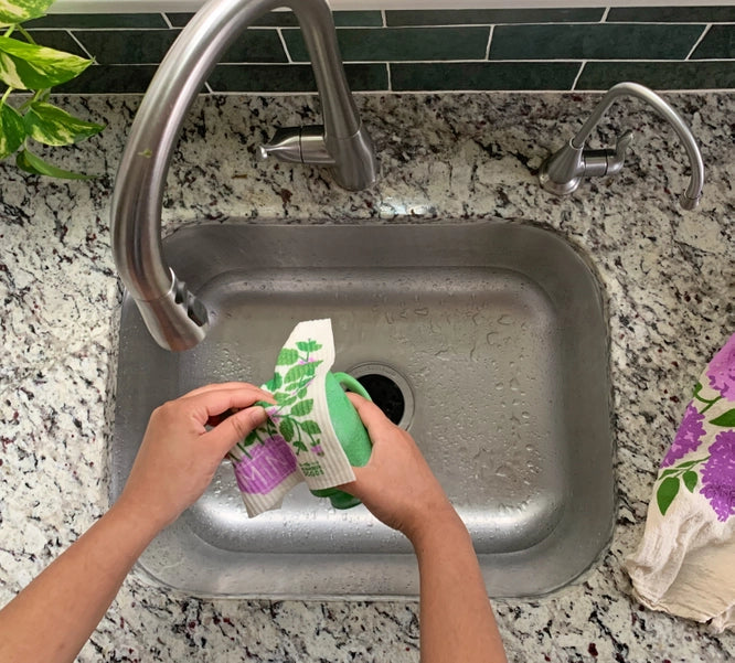 Mint sponge cloth being used to wash a green mug at the sink.