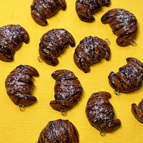 Several chocolate croissant charms laying flat on a yellow backdrop