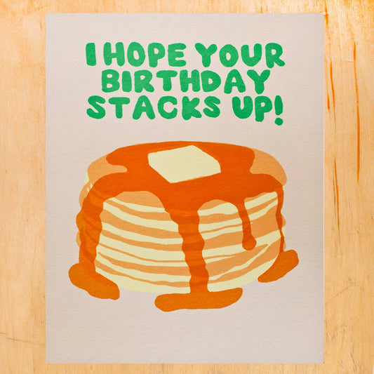 birthday greeting card that has an illustration of a stack of pancakes with syrup and butter on top. Text reads "I hope your birthday stacks up!"