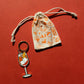 Keychain with an aperol spritz design and a small drawstring bag on a red background