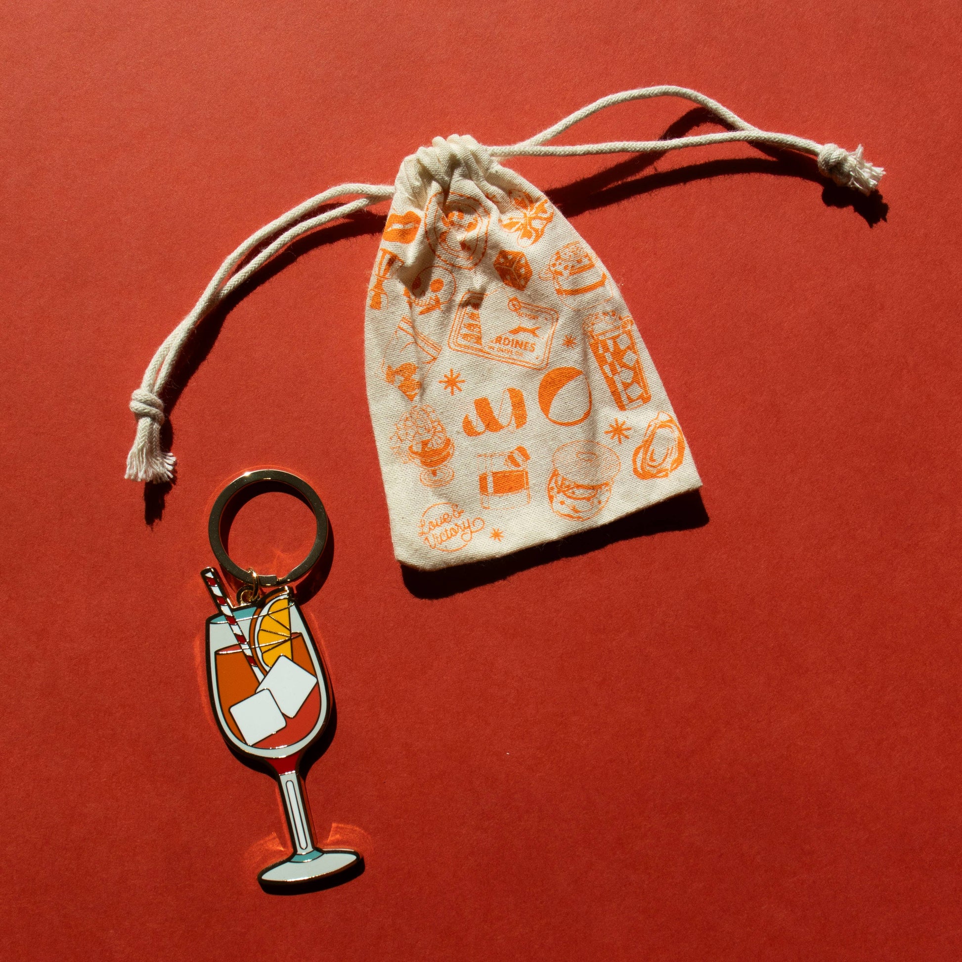 Keychain with an aperol spritz design and a small drawstring bag on a red background
