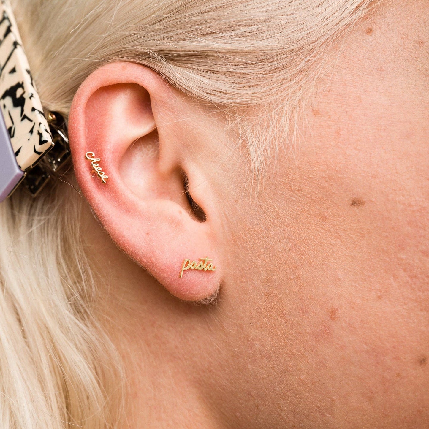 Single 14k gold plated stud earring on ear -- reads "cheese" and "pasta" in handwritten script