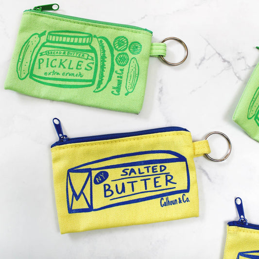Green pickle zipper pouch along with a yellow and blue salted butter zipper pouch 