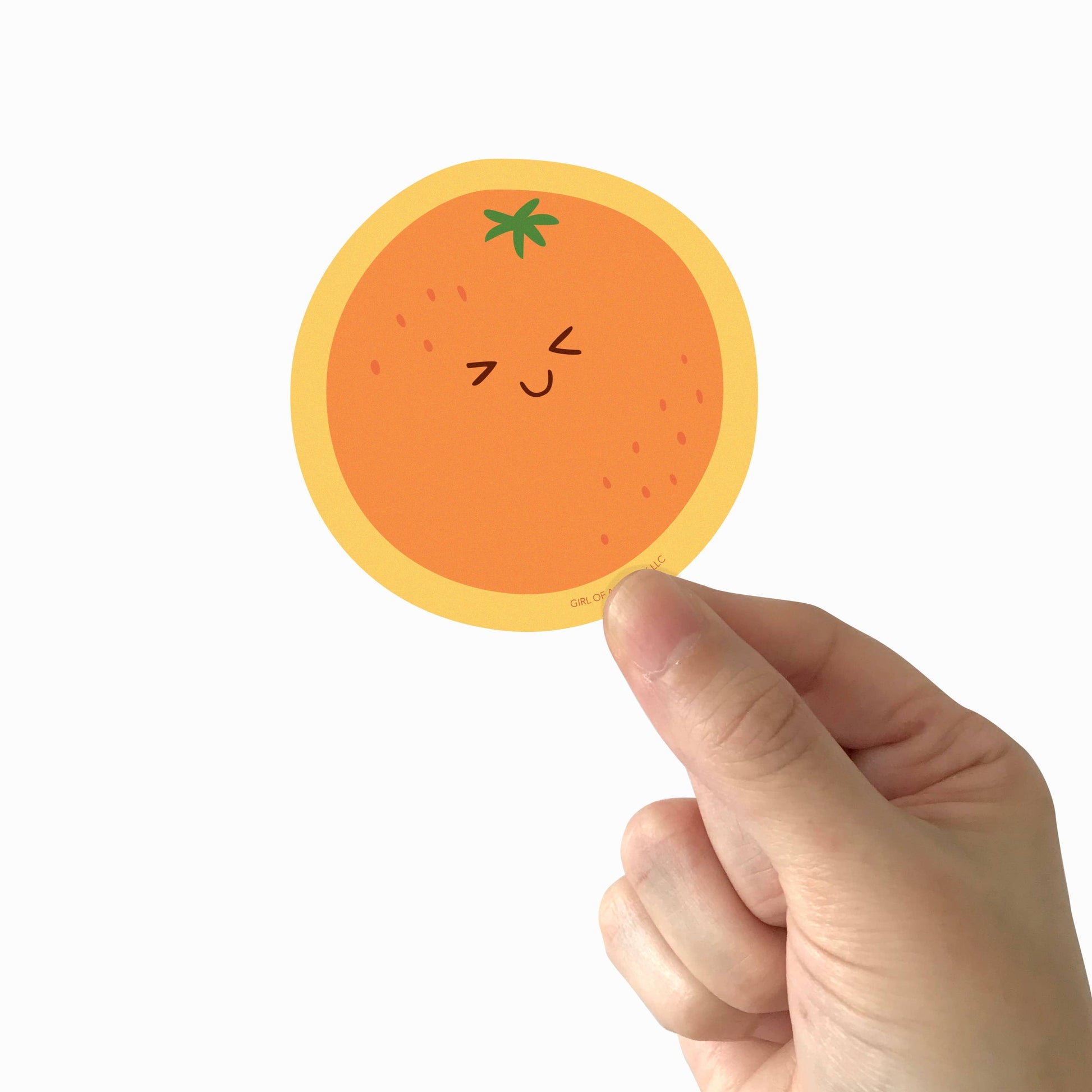 Vinyl sticker of an orange making a cute, smiley face, being held in someone's hand 