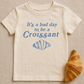 Beige t-shirt with blue text and croissant graphic on a beige background