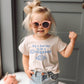 Child wearing pink sunglasses and a t-shirt with a humorous message "it's a bad day to be a croissant" 