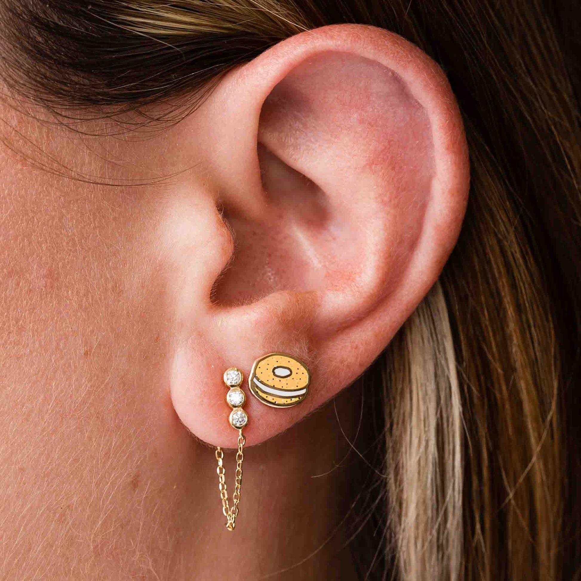Close-up of an ear wearing a stud earring made to look like a bagel with schmear