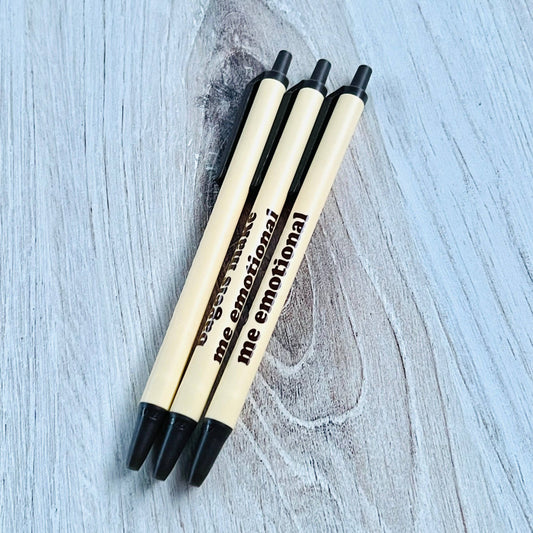 Three pens with black and beige design on a light wooden surface. Text on them read "bagels make me emotional" 