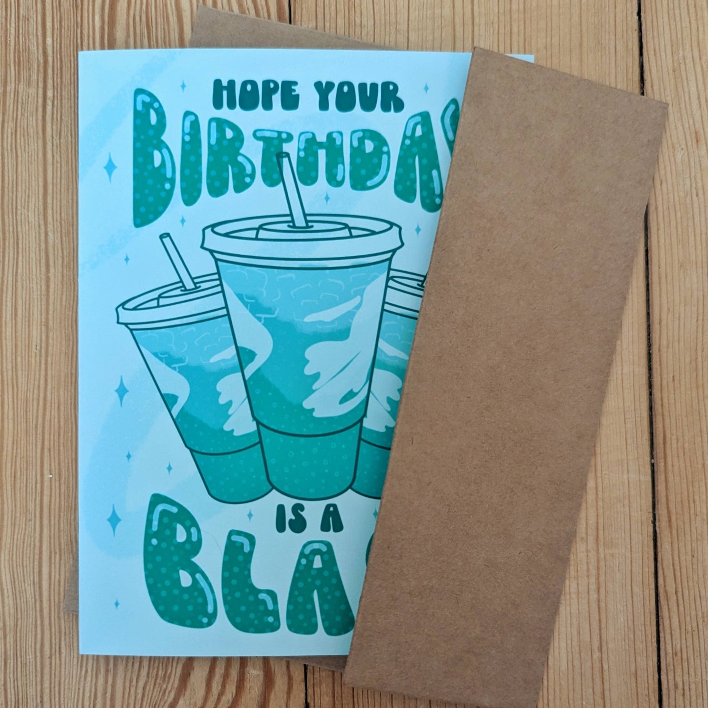 Birthday card with baja blast cups design and brown envelope on a wooden surface