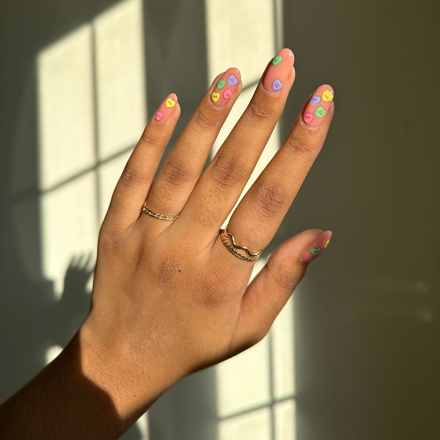 Hand with colorful nail designs using the candy heart nail stickers against a window with sunlight casting shadows.