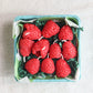 Red raspberry-shaped candles in a box on a light gray background