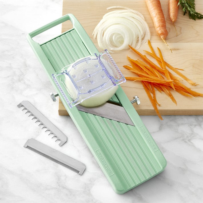 Benriner green mandoline with attachments and finger guard. Picture displays a white onion being sliced and a carrot already julienned. 