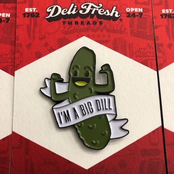 Enamel pin of a dill pickle flexing it's muscles. Text on a white banner reads "I'm A Big Dill" 