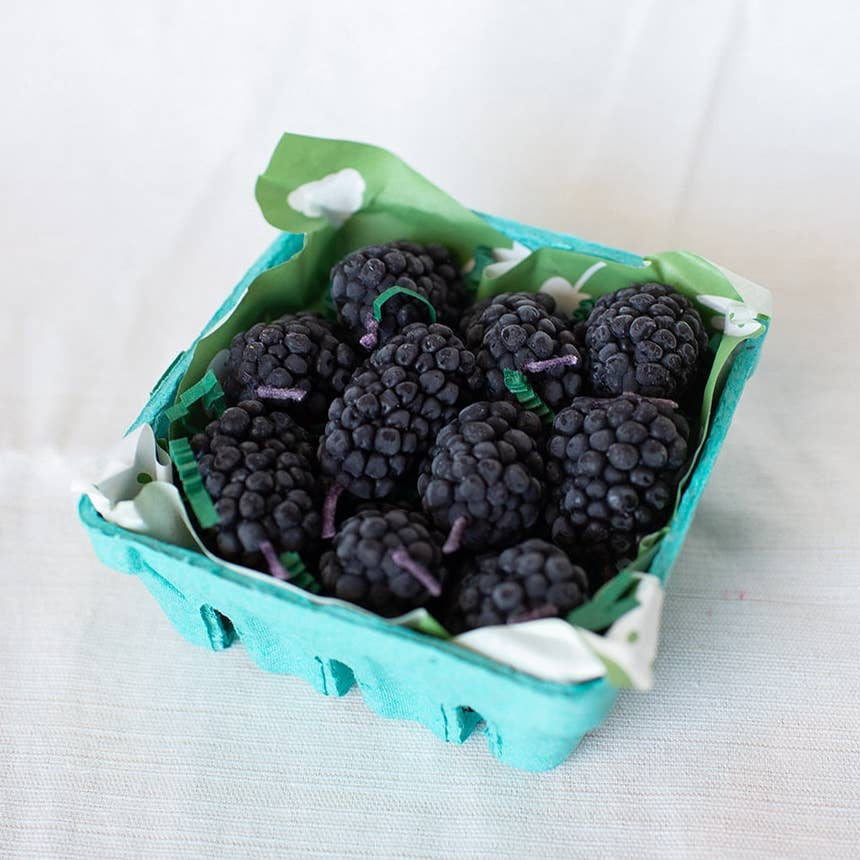 Green container filled with blackberry shaped candles on a light background