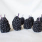 Blackberry shaped candles arranged in a row on a white background