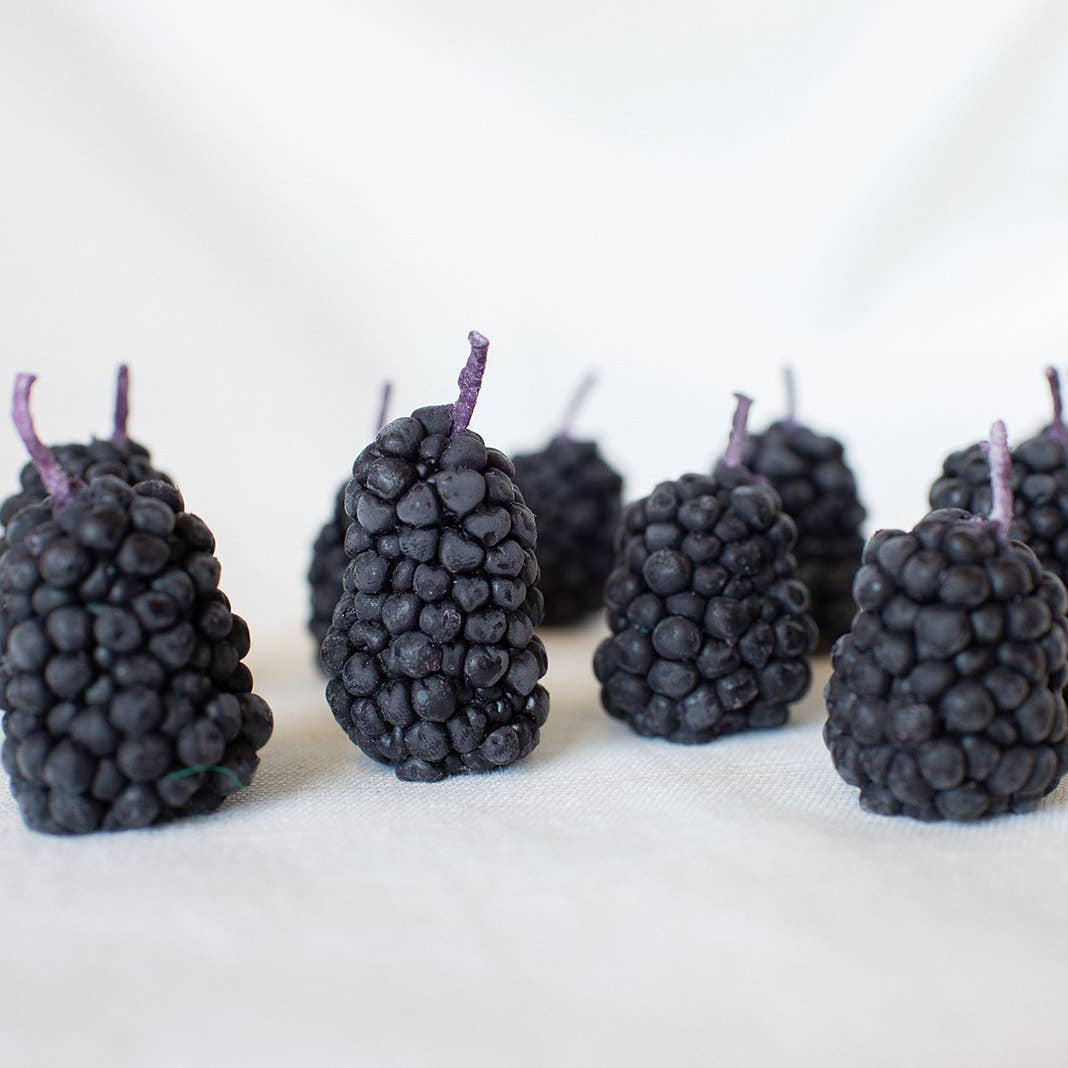 Blackberry shaped candles arranged in a row on a white background