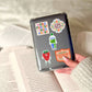 Person holding a clear case with stickers over an open book