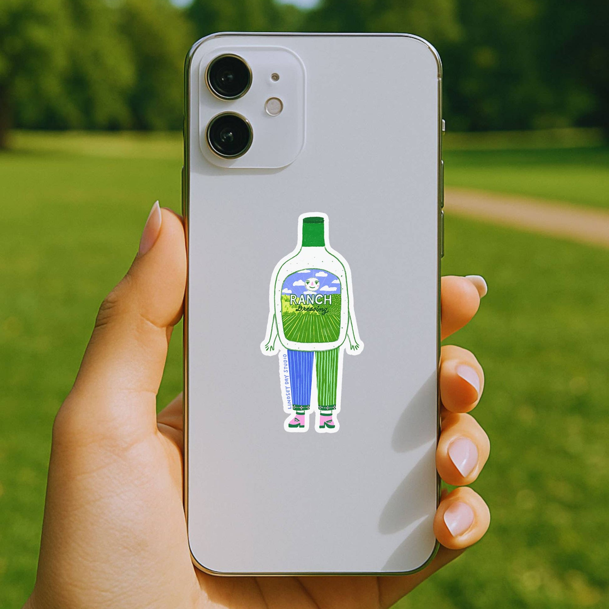 Phone case with a cartoon character sticker held by a hand outdoors
