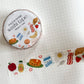 A roll of Peach & Papirie washi tape with a cute breakfast-themed pattern, shown next to a strip of the tape unrolled on a white grid notebook.