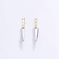 Pair of knife-shaped earrings with gold handles and silver blades on a light purple background