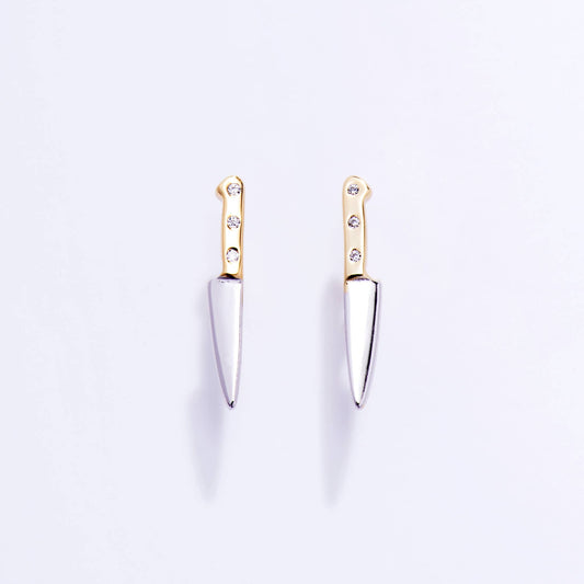 Pair of knife-shaped earrings with gold handles and silver blades on a light purple background