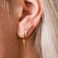 Close-up of a person wearing a butcher knife shaped earrings with gold handles and a silver blade 